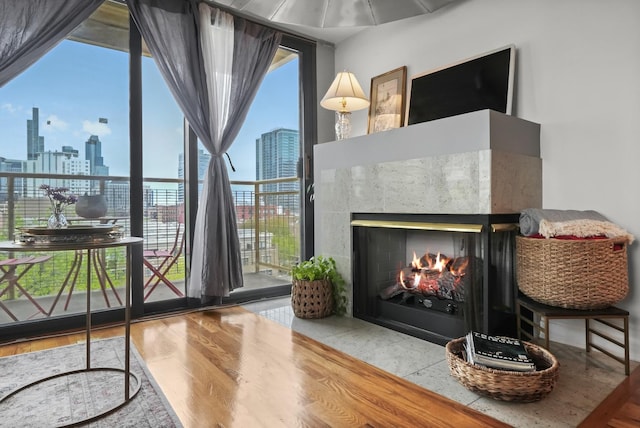 living room with a city view, a tiled fireplace, expansive windows, and wood finished floors