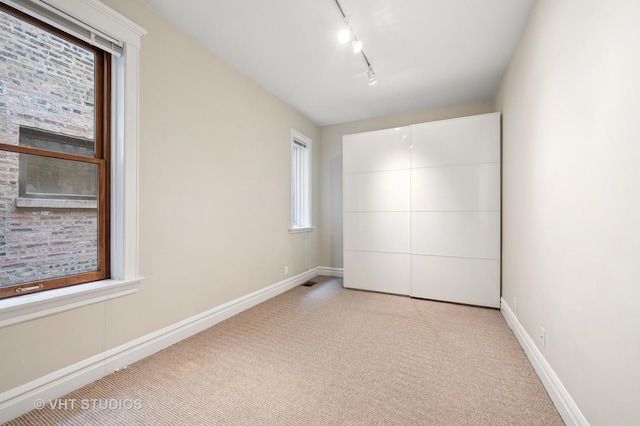 unfurnished bedroom featuring rail lighting, light carpet, and baseboards