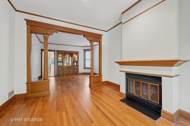 unfurnished living room featuring decorative columns, wood finished floors, baseboards, a fireplace with flush hearth, and crown molding
