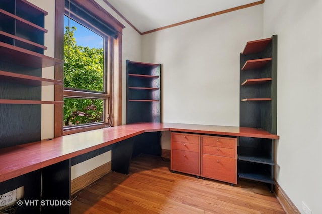 unfurnished office with ornamental molding, built in desk, light wood-style flooring, and baseboards