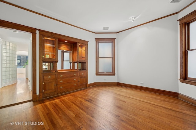 empty room featuring light wood-type flooring, baseboards, and crown molding