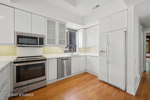 kitchen with stainless steel appliances, a sink, light wood finished floors, white cabinetry, and recessed lighting