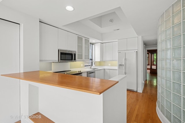 kitchen featuring appliances with stainless steel finishes, a raised ceiling, a sink, light wood-style flooring, and white cabinets