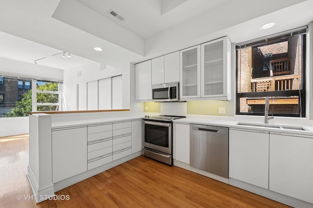 kitchen with stainless steel appliances, a sink, white cabinets, light wood-style floors, and light countertops