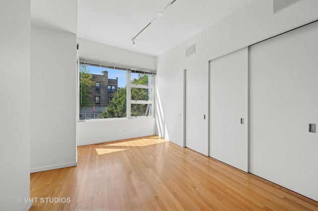 unfurnished bedroom featuring track lighting, hardwood / wood-style floors, baseboards, and a closet