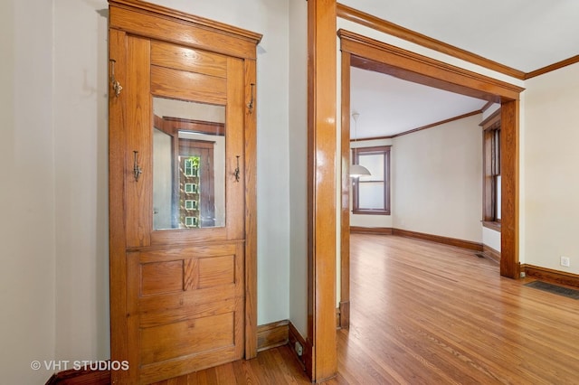 hallway with ornamental molding, wood finished floors, baseboards, and plenty of natural light