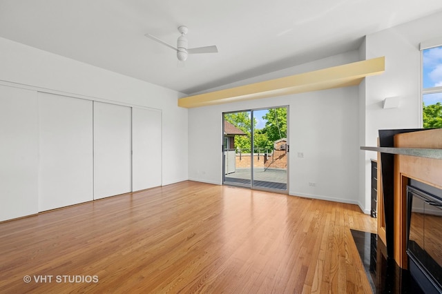 unfurnished living room with light wood-type flooring, a fireplace with flush hearth, healthy amount of natural light, and a ceiling fan