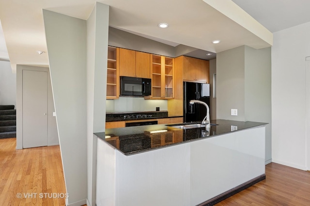 kitchen featuring black appliances, open shelves, a peninsula, dark stone countertops, and light wood-style flooring