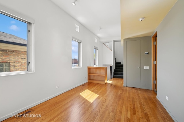 unfurnished room with light wood finished floors, stairway, and baseboards
