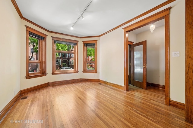 empty room with wood-type flooring, baseboards, track lighting, and ornamental molding