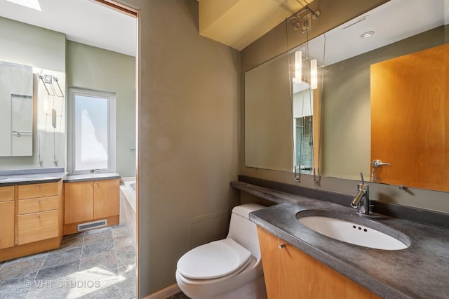 bathroom featuring toilet, two vanities, and a garden tub