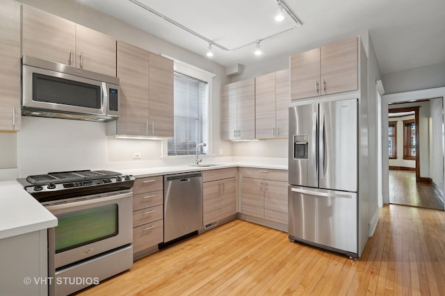 kitchen with stainless steel appliances, a sink, light wood-style floors, and light countertops