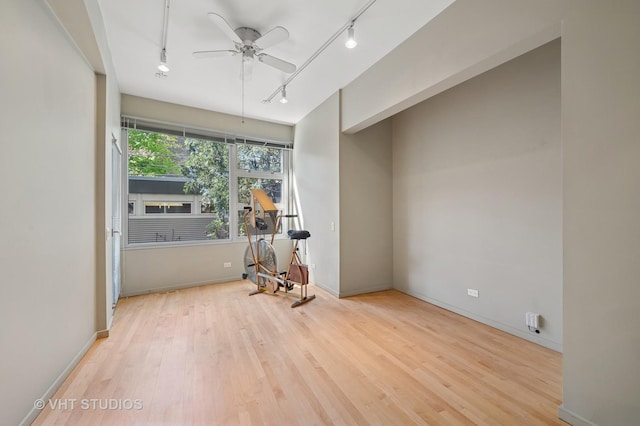empty room with rail lighting, wood finished floors, ceiling fan, and baseboards