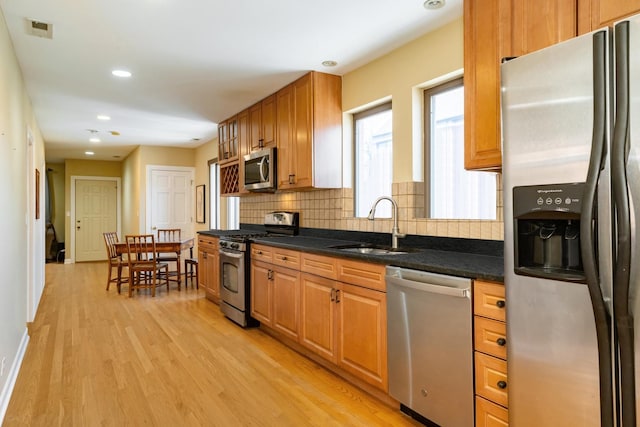 kitchen with appliances with stainless steel finishes, a sink, decorative backsplash, light wood-style flooring, and recessed lighting