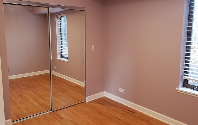 unfurnished bedroom with light wood-style flooring, a closet, baseboards, and multiple windows