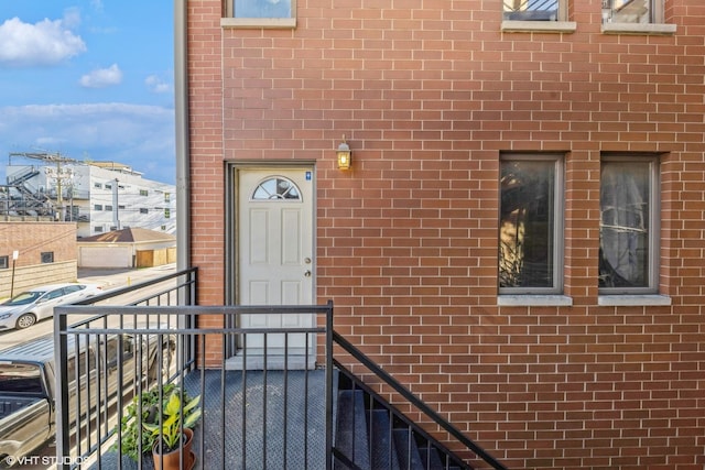 view of exterior entry featuring a balcony and brick siding
