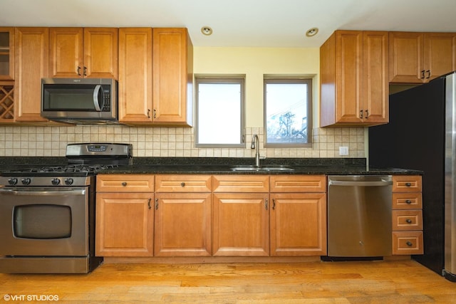 kitchen featuring appliances with stainless steel finishes, a sink, light wood finished floors, and brown cabinets