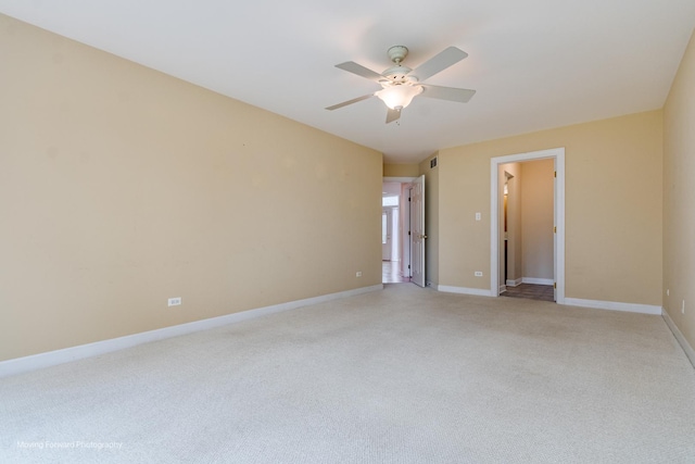 spare room featuring light carpet, a ceiling fan, and baseboards