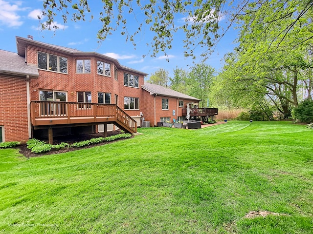 rear view of property featuring a deck, brick siding, a yard, and cooling unit