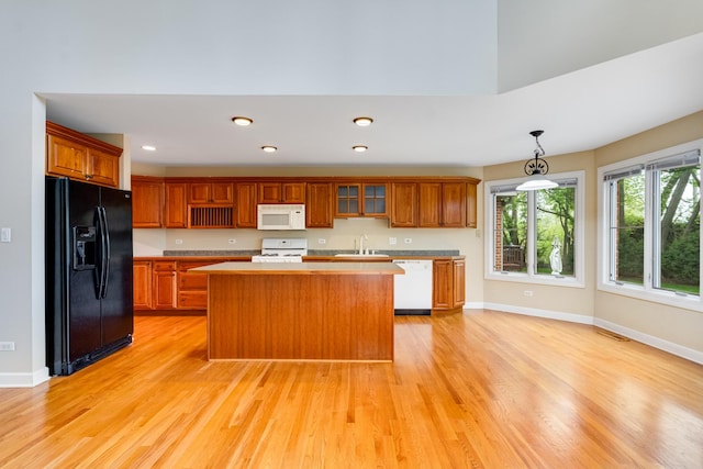kitchen featuring white appliances, a sink, light countertops, a center island, and light wood-type flooring