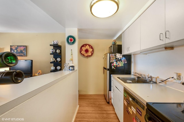 kitchen with appliances with stainless steel finishes, a sink, light wood-style flooring, white cabinets, and baseboards