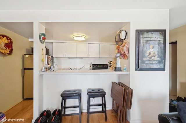 kitchen with light wood finished floors, freestanding refrigerator, black electric range oven, white cabinetry, and a peninsula