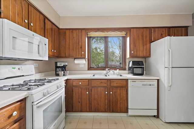 kitchen with white appliances, a sink, brown cabinetry, and light countertops