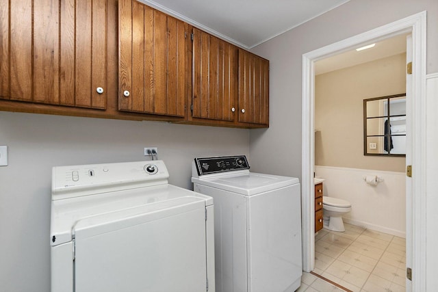 laundry area featuring washing machine and dryer, cabinet space, wainscoting, and crown molding