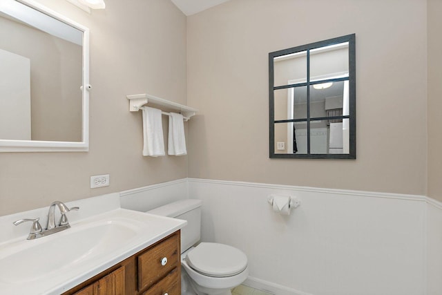 bathroom with toilet, vanity, and a wainscoted wall