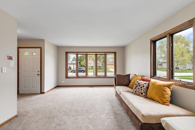 living area featuring healthy amount of natural light, light colored carpet, and baseboards