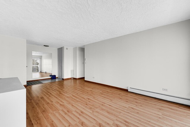 unfurnished living room with wood finished floors, a textured ceiling, a baseboard heating unit, and baseboards