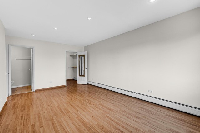 unfurnished bedroom with a baseboard radiator, a spacious closet, light wood-type flooring, recessed lighting, and baseboards