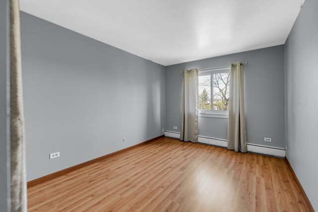 spare room with light wood-style flooring, baseboards, and a baseboard heating unit