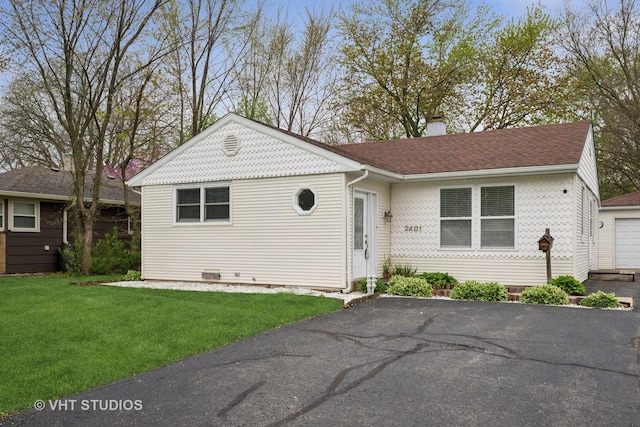 ranch-style home featuring aphalt driveway, roof with shingles, a front lawn, and a chimney