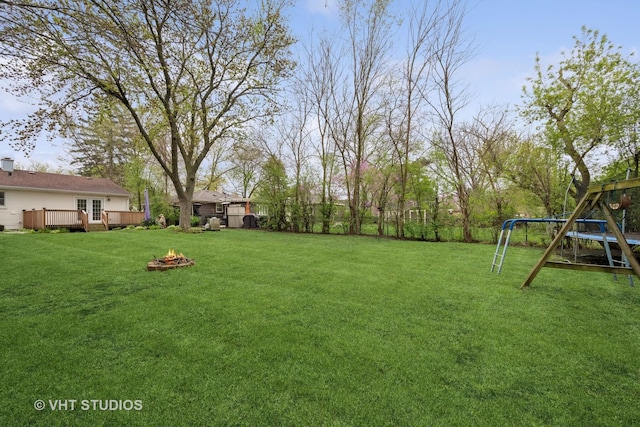 view of yard with an outdoor fire pit, a deck, a fenced backyard, and a playground