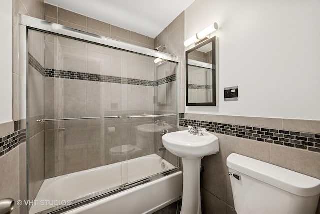 full bathroom featuring combined bath / shower with glass door, toilet, and tile walls