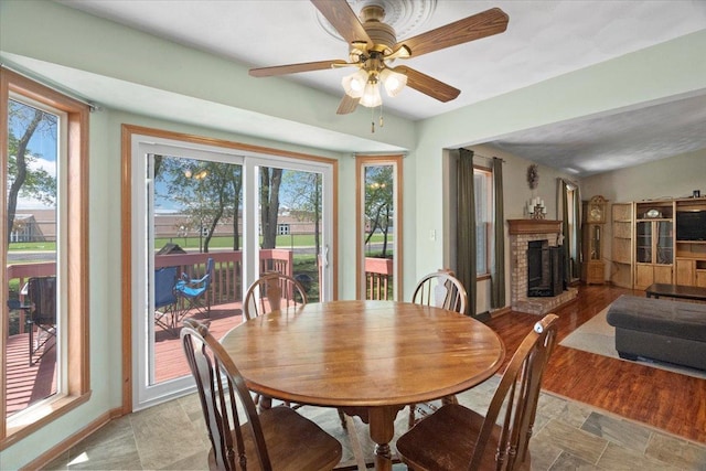 dining area with stone finish flooring, a fireplace, ceiling fan, and plenty of natural light