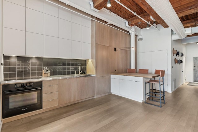 kitchen with black oven, modern cabinets, light wood-style flooring, light countertops, and tasteful backsplash