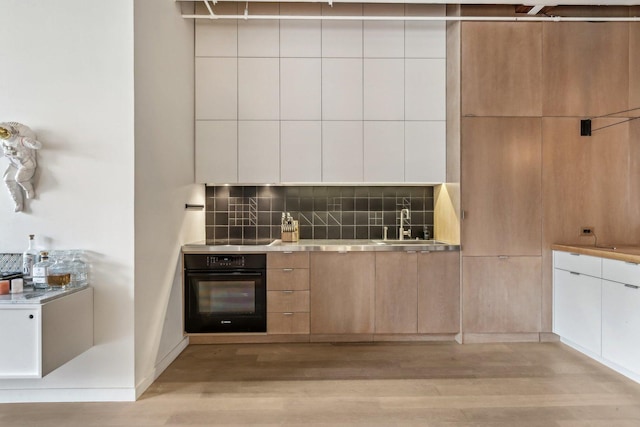 kitchen featuring black oven, modern cabinets, light wood-style floors, tasteful backsplash, and a sink