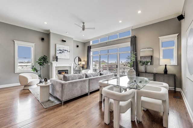 living room with a ceiling fan, baseboards, a glass covered fireplace, light wood-style floors, and ornamental molding
