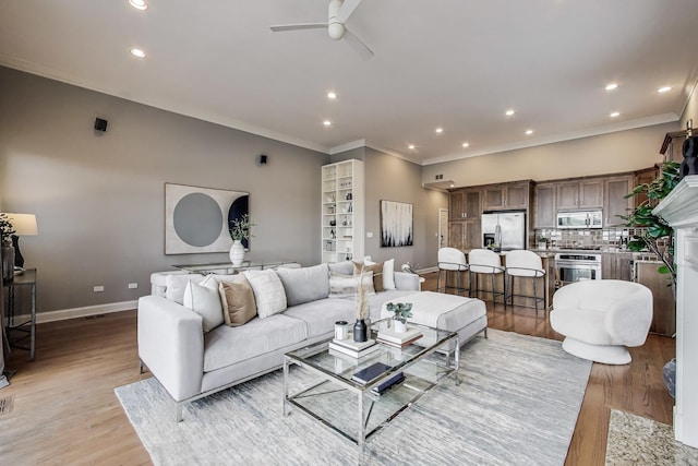 living area with a ceiling fan, light wood-style flooring, ornamental molding, baseboards, and recessed lighting