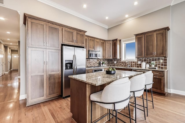 kitchen with stainless steel appliances, ornamental molding, a kitchen island, light wood-style floors, and backsplash