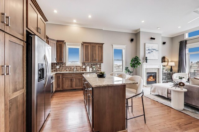 kitchen featuring stainless steel refrigerator with ice dispenser, open floor plan, a kitchen breakfast bar, a center island, and crown molding
