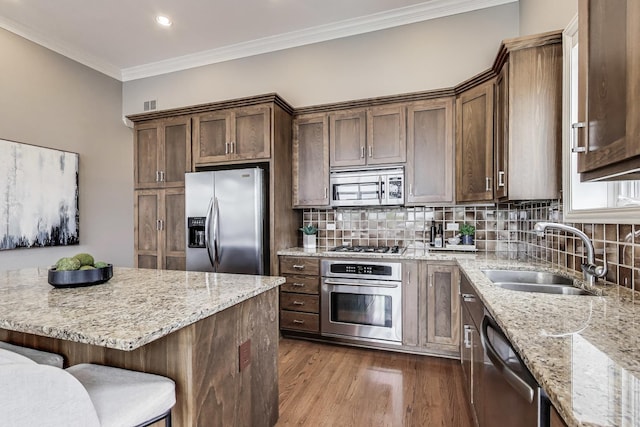kitchen featuring appliances with stainless steel finishes, a sink, dark wood finished floors, a kitchen bar, and light stone countertops