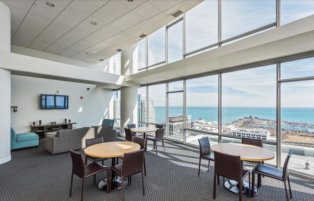 carpeted dining area featuring a towering ceiling, a water view, and a healthy amount of sunlight