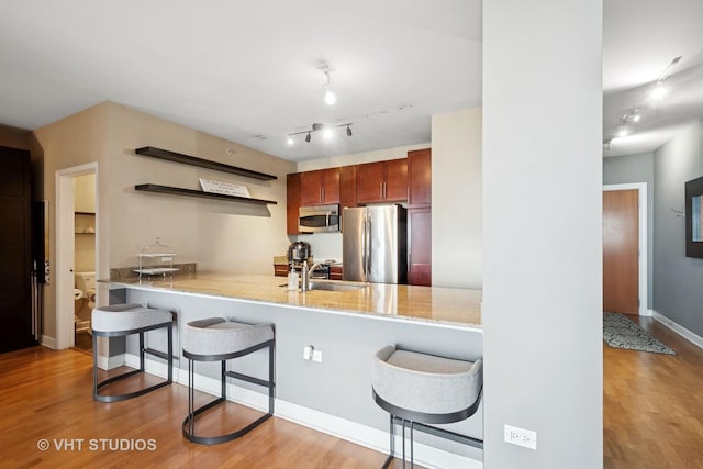 kitchen with a sink, appliances with stainless steel finishes, open shelves, and wood finished floors