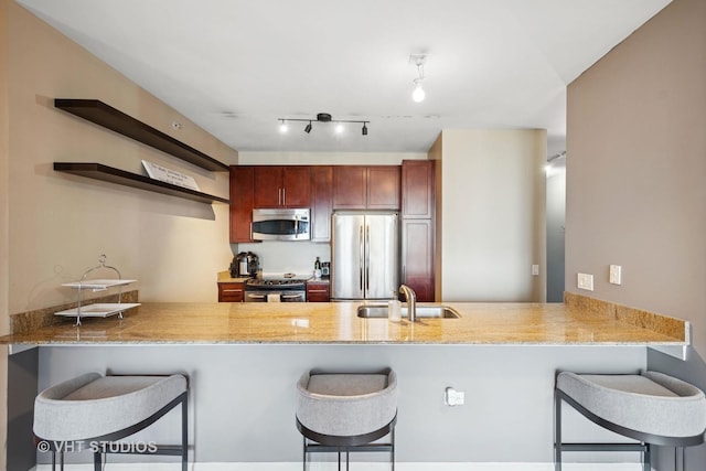 kitchen with light stone countertops, appliances with stainless steel finishes, a sink, a breakfast bar area, and a peninsula
