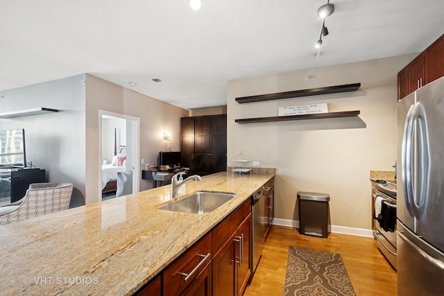 kitchen with open shelves, appliances with stainless steel finishes, light stone countertops, a sink, and light wood-style flooring