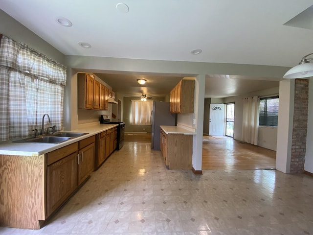 kitchen featuring range with electric stovetop, a sink, light countertops, brown cabinetry, and freestanding refrigerator