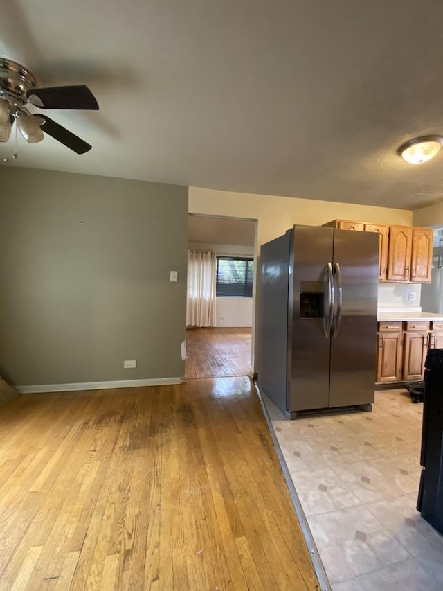 kitchen featuring stainless steel fridge with ice dispenser, a ceiling fan, light wood-type flooring, light countertops, and baseboards